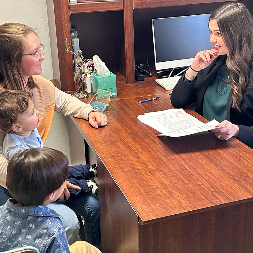 A woman and two children sit across from another woman holding papers in an office setting.
